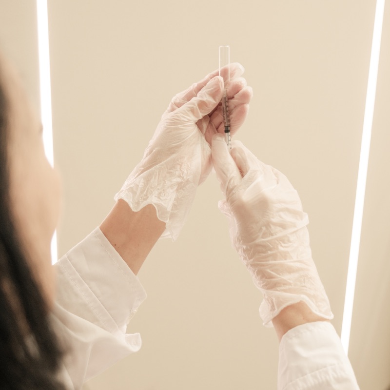 Profissional de luvas preparando uma seringa com injetável em sala de procedimento